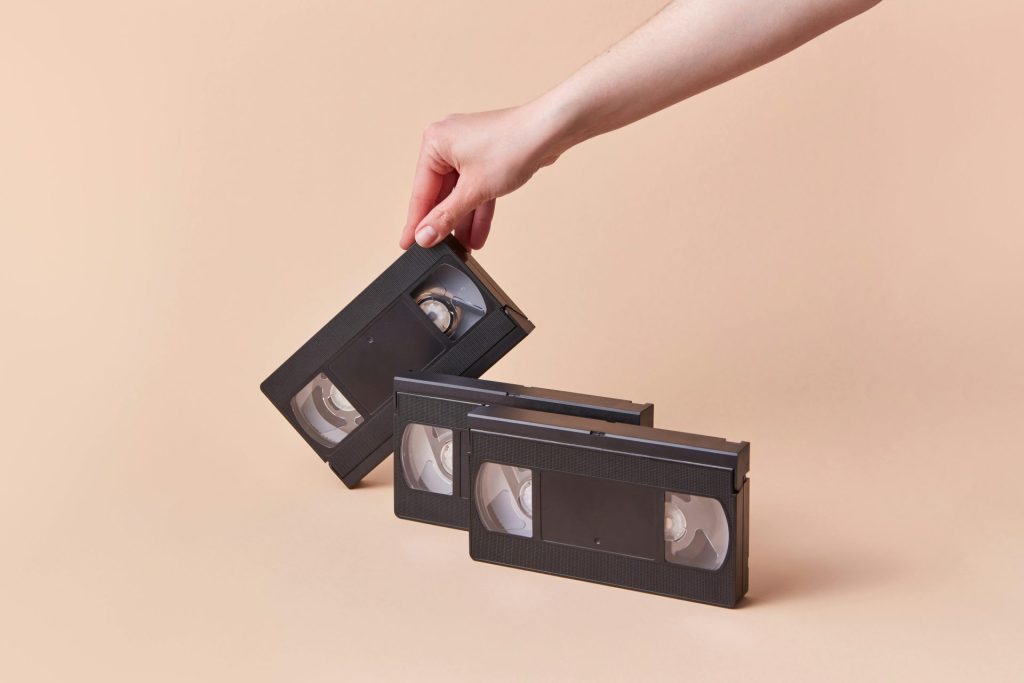 Hand holding a vintage VHS tape with a retro collection against a beige background.